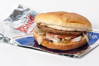 Photo of a Sonic Junior Deluxe Burger. The burger is wresting on top of its wrapper with a plain white background.