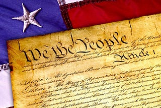 Photo of the heading We the People of the Constitution of the United States of America atop an American flag.