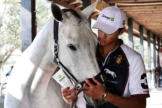 Timmy Dutta stands with a white polo pony, wearing a Zarasyl hat and holding a tube of Zarasyl.