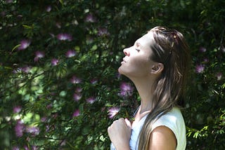 Young woman seen from the side, her face lit by the sunlight. Flowers bloom in the background.