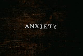 The word “Anxiety” spelled out in white letters lying on a dark brown wooden table.