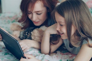 Image of a woman and a younger girl smiling and looking at a tablet