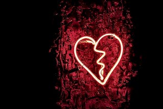 A glowing light red neon heart displayed against a dark red background.