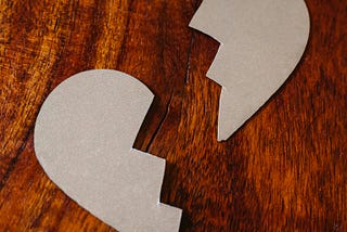 A cardboard heart shaped object broken in two on a wooden table