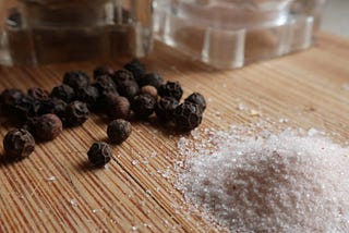 close-up of black peppercorns next to pink himalayan salt on bamboo cutting board