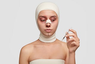 Mulher branca realizou uma rinoplastia, ela está olhando para uma seringa que segura na mão e apresenta pontos pintados no rosto para realizar novas cirurgias plásticas.
