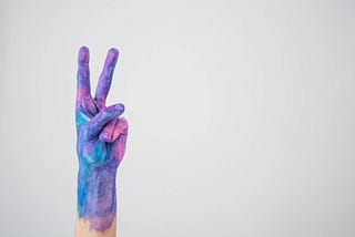 A hand painted purple, pink and blue throwing up a peace sign