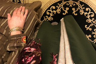 Two women are shown praying on a carpet beside each other. One is standing, the other is sitting.