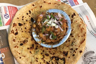 A plate of chole on top of chapati wrapped in newspaper.