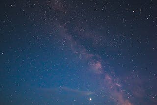 A night-sky showing star-fields and dark land below