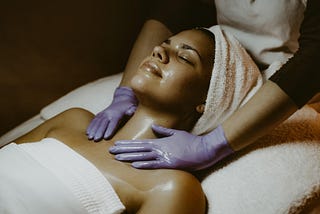 Picture of a black woman in a towel receiving a massage from a gloved professional