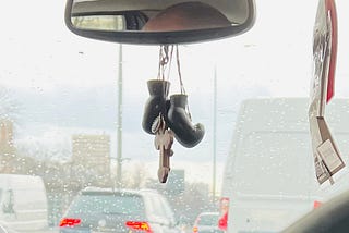 A big wooden cross and a pair of mini boxing gloves hanging from a rearview mirror