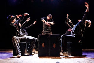 Five improv performers strike bold poses on a dark stage.