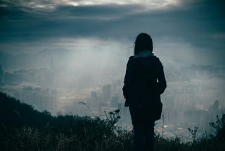 Silouette of woman standing on a hill looking at bleak landscape.