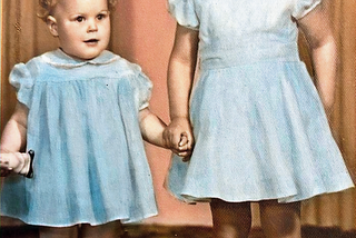Mid-1950s studio photo of two girls, aged about 4 and 2, wearing blue dresses and holding hands.