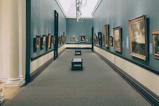 A narrow corridor in an art gallery with pictures hanging on all the walls.