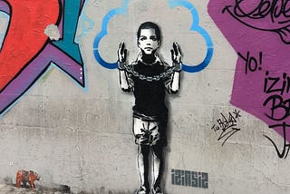 Graffiti of a boy with his hands raised in handcuffs and a cloud outline encircling his head representing ideas.