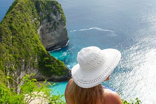 Picture of writer facing away, sitting at the edge of Kelingking Beach, Bali, Indonesia.
