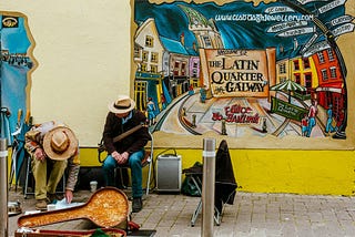Two musicians looking at music near a colorful mural that reads The Latin Quarter of Galway.