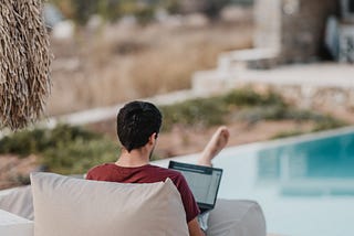 A digital nomad sits behind his laptop overlooking a swimming pool