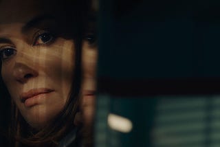 A woman peers at us through shadows.