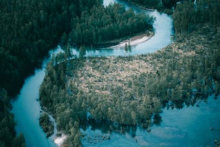 A beautiful aerial photo of a vivid blue river bordered by thick, green forests.