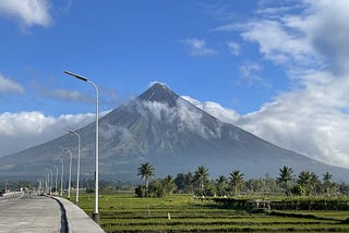 View of a volcano overlooking a rice-field and half of the paved road