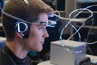 A person wearing a sleek, silver BCI headset with glowing electrodes focused on a computer screen.