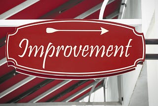 Red store sign that says “Improvement” in script with an arrow pointing to the right