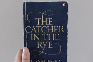 Fariza’s hand holding The Catcher in the Rye book in front of a cream colored background