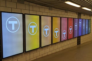 A line of ad displays with each screen a different color and the MBTA logo