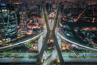 Night time view from the sky of bridge and surrounding city, with lights shining all around.