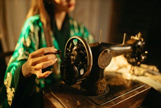 An old sewing machine, with the obscured figure of a woman operating it.