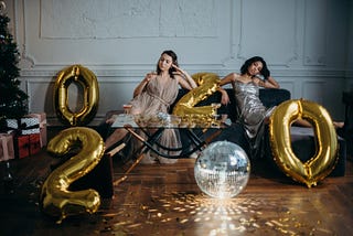 What to do when your New Year’s resolutions fail. Image: Women on couch drinking wine surrounded by large year 2020 balloons.