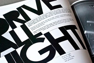 Black and white photograph of a professionally designed book. The words ‘drive all night’ is the title and are designed and laid out creatively and take up a majority of the left side of the spread (the right right of the spread is not shown muchbut appears to be a black and white photograph of a concert). The lyrics are small and in a sans serif typeface and housed within blank space between the title.