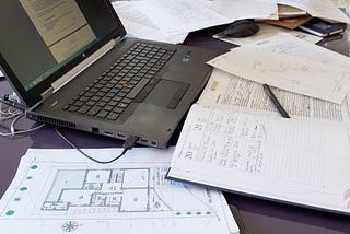 Imagem de uma mesa de trabalho com computador, projetos de arquitetura e anotações, de 2017 por Thaís Kamigashima