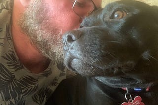 Man leaning in to nuzzle a black dog