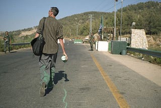 A man walking with a leaking can of green paint at the street