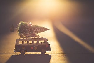 Picture depicts a toy van with a tiny Christmas tree strapped to the roof.