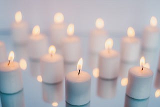 the photograph shows 12 lit white candles against a white backdrop