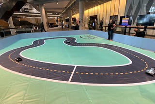 A miniature-sized car racing track with a single loop of road with remote control cars moving in the same direction.