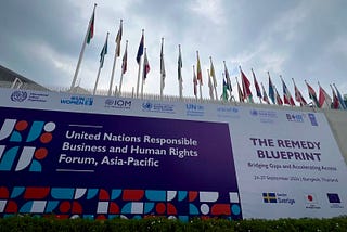 Sign reading United Nations Responsible Business and Human Rights Forum, Asia-Pacific in front of a row of flags in the entrance to the UN Building in Bangkok