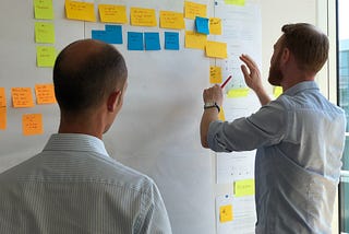 Two men working on a whiteboard full of Post-it notes