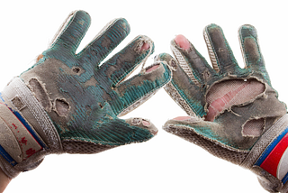 Two hands with worn out soccer gloves.