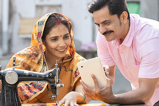 A man and woman sit at a table with a sewing machine, showcasing the impact of digital marketing on India’s rural communities.