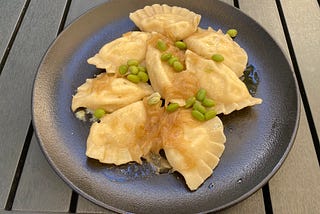 A plate of delicious pierogie ruskie, topped with fried onion and edamame beans