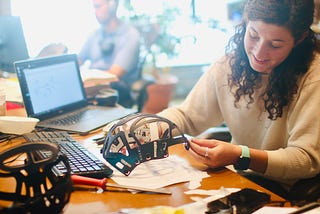 White woman, brown hair, and student holding model and sketch of a helmet.