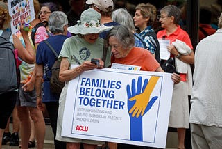 Two people with a “Families Belong Together” sign at an ACLU rally 1 June 2018