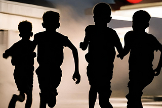Silhouettes of four boys running away from a gas station at night.