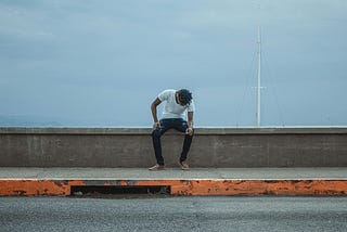 A man, head down, sitting on a concrete barrier